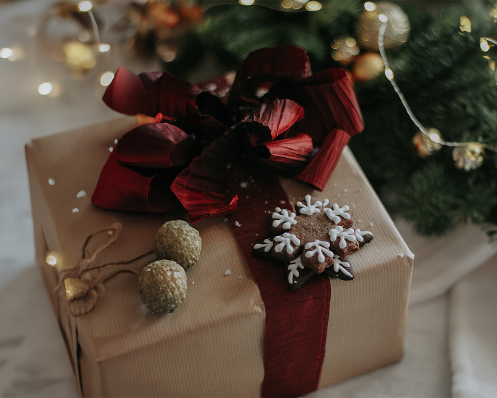 Vánoční dárek zabalený do papíru, převázaný mašlí a ozdobený cukrovím.