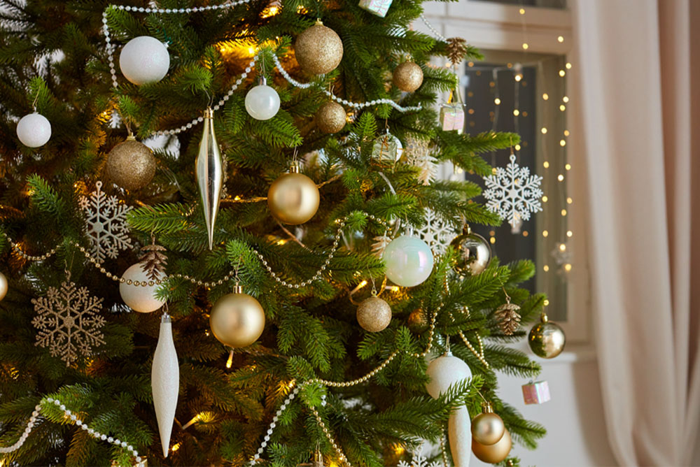 Vánoční stromek s ozdobami ve zlaté, stříbrné a bílé barvě.