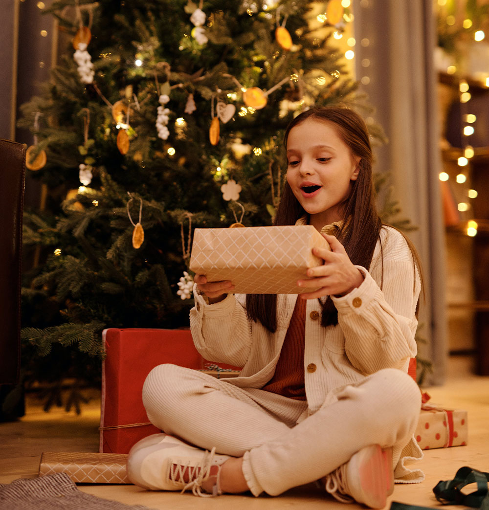 Dívka se těší z dárku pod vánočním stromkem.