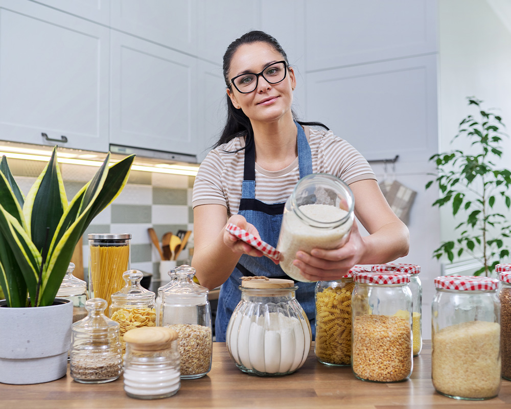 Žena v kuchyni ukazuje sklenice na skladování suchých potravin