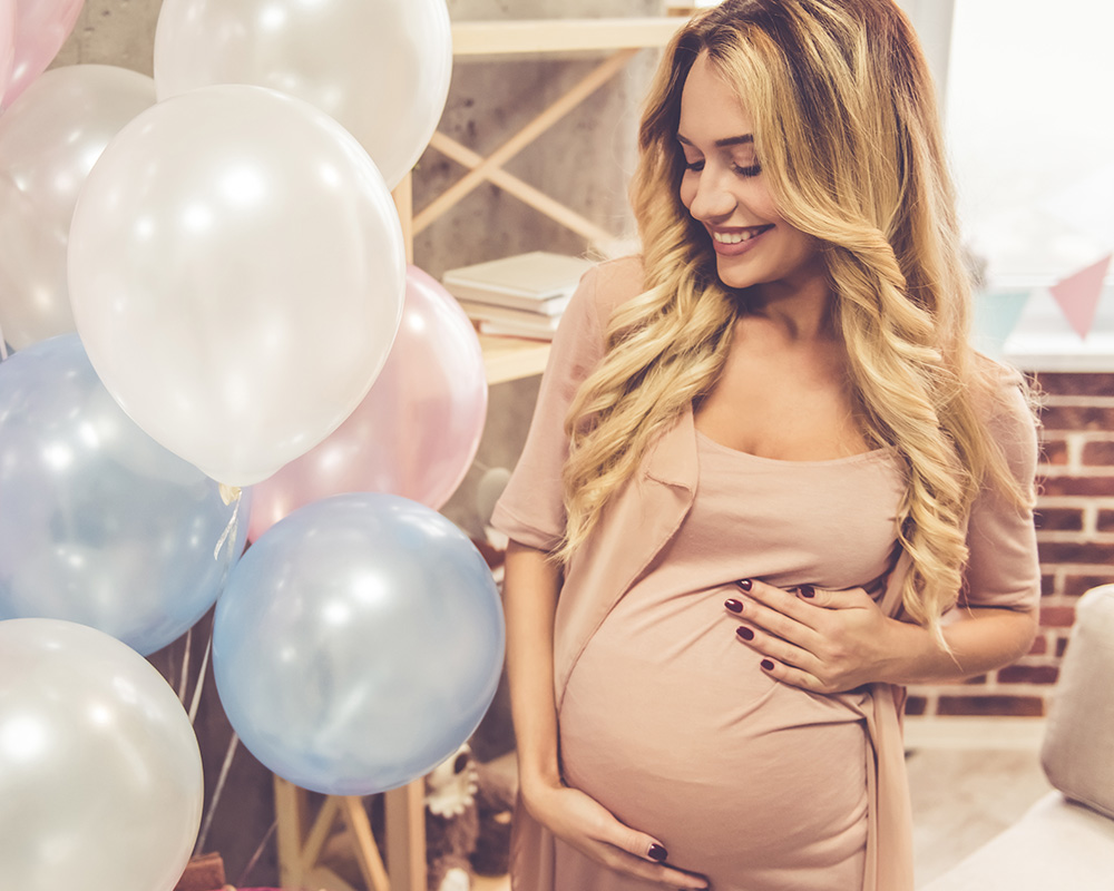 Těhotná žena se s úsměvem dívá na barevné balónky na oslavě baby shower