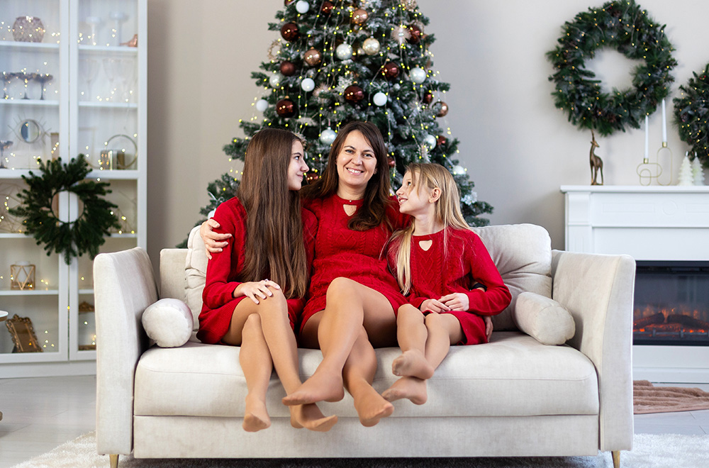 Maminka a její dcery v červených šatech tráví sváteční čas spolu u vánočního stromku.